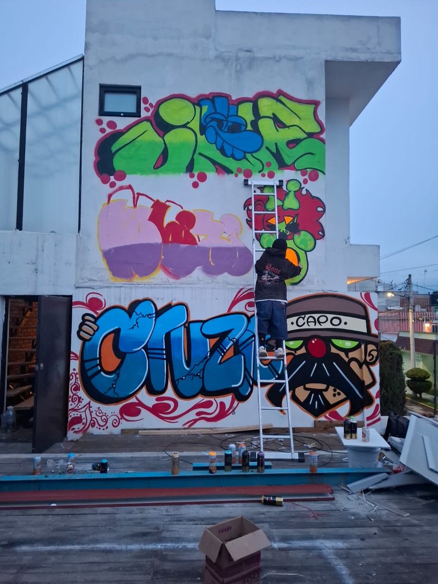 Cruzie pintando de pie sobre una escalera, terminando su firma junto al rostro de Capo.