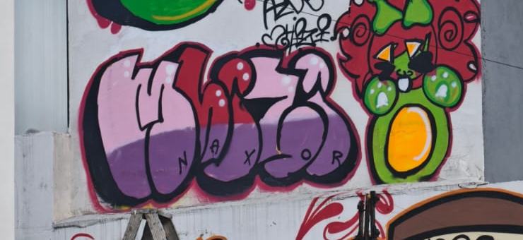 Letras de graffiti en morado y rosa, firmadas Naxor.