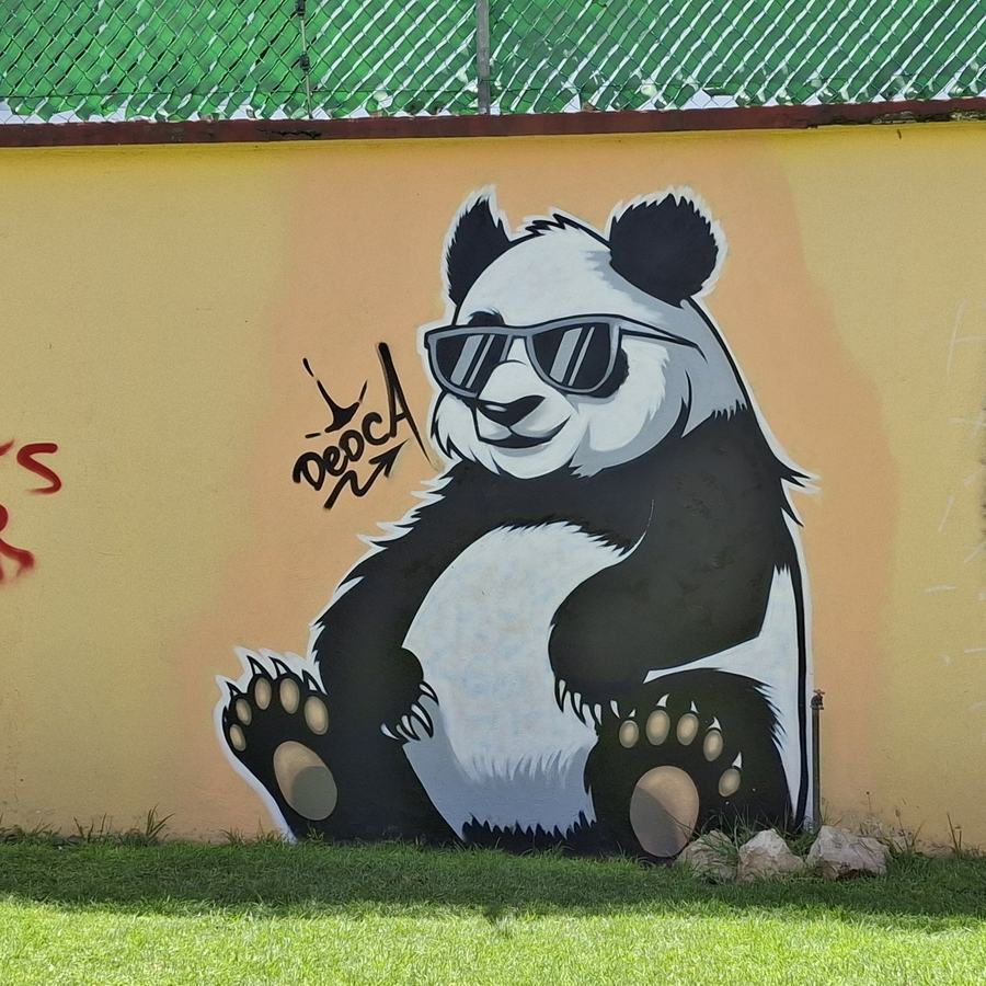 Mural de un panda con lentes oscuros pintado por Dedca sobre la barda amarilla de Canvas 90.