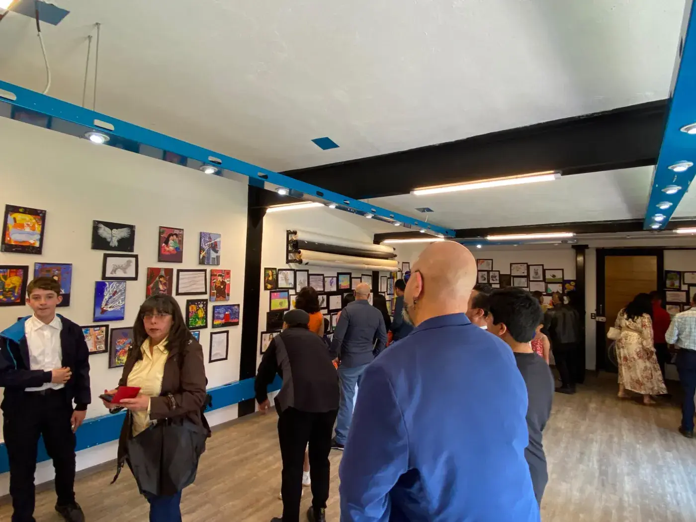 Visitantes viendo de cerca los dibujos y pinturas de los alumnos en la pared de Canvas 90.